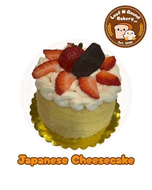 A decorated Japanese cheesecake from Loaf N Round Bakery, topped with whipped cream, fresh strawberries, a chocolate piece, displayed on a gold scalloped base against a white background with the bakery logo and 'Japanese Cheesecake' text.