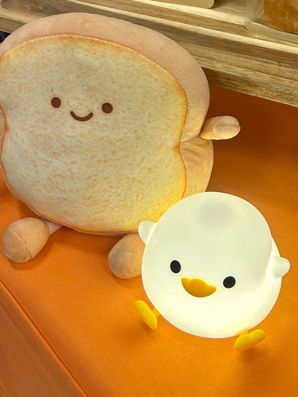 A tabletop display featuring a plush toy bread character, and a small glowing duck-shaped lamp on an orange tablecloth.